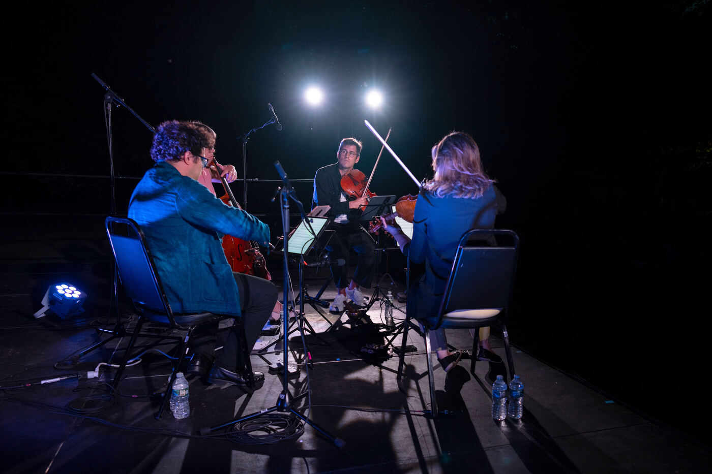 The quartet seated in near-total darkness, two stage lights hanging above them like moons.