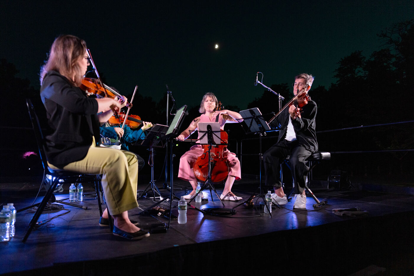 The Attacca Quartet playing at night with the moon visible in the sky above them.